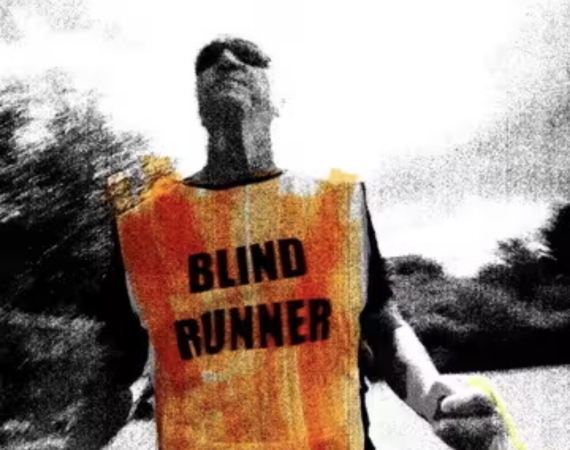 A fisheye camera angle points back at Phil, a blind runner. He wears a bright orange hi-vis tabbard with ‘blind runner’ in large capitals, dark wrap-around sunglasses and clutches a luminous yellow tether that connects him to his guide runner. The whole image is treated with a high-contrast, punk-inspired photocopy texture in black and white, with the accent colours roughly scribbled on top with a highlighter marker.