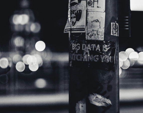 A black and white image of a lamp post with text written on it - the text reads "Big Data is Watching You", and is written on the lamp post with white ink on the black structure. 