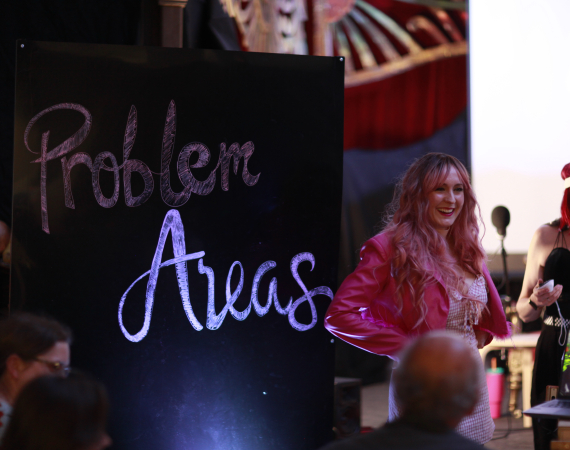 A woman stands in front of a sign reading "Problem Areas"