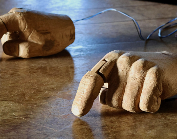 Two mechanical hands, made of wood, on a wooden table.