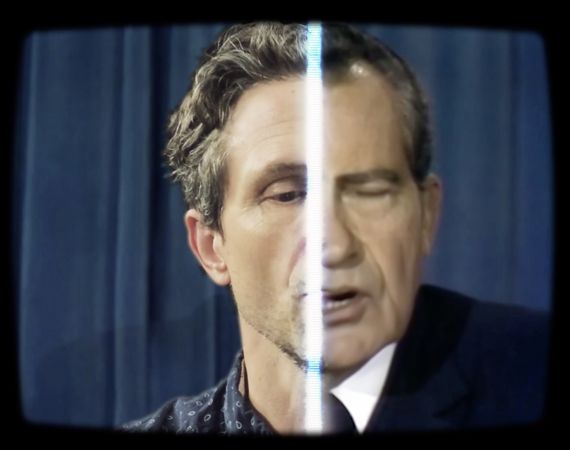 distorted image of a male with a stripe of light through the face to separate the left and the right side. The image has a blue background and black tv effect to frame the image