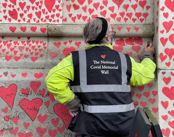 an image of a person faced towards the national Covid Wall that is covered in red hand drawn love hearts.