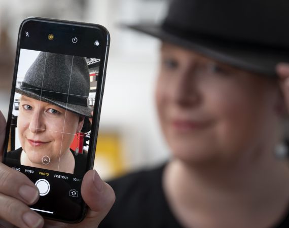 meriko holding an iPhone and taking a picture of herself with her face blurred in the background and also seen on the iPhone screen. 