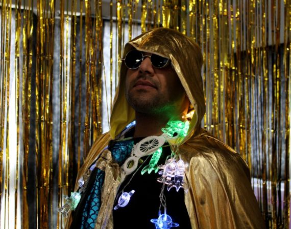 An image of Tony Bhajam, the Watershed Inclusion Officer wearing a gold cape and fairy lights around his neck, and a pair of sunglasses, looking into the distance.