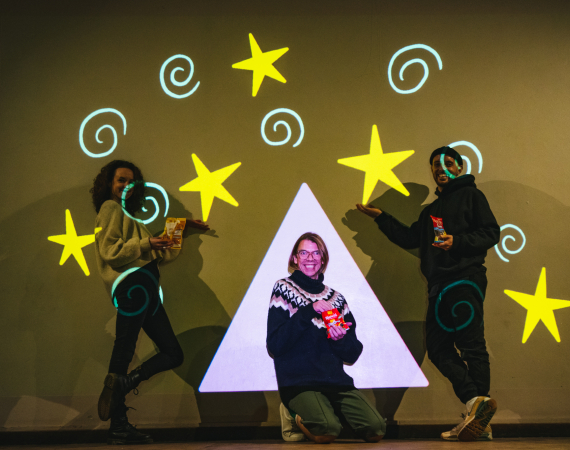 Team of three people smiling and pausing in front of colourful projected drawing