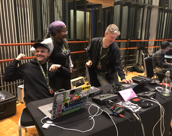 Several people sitting at audio works stations surrounded by audio equipment in Real World's Recording Studio.