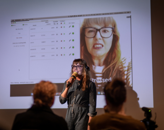 Photo of Victoria Melody holding a mic talking to an audience.