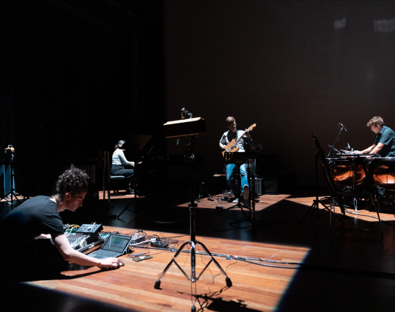 Image of Craig Scott performing with other musicians in dark space, lit in the centre.