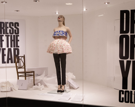 Mannequin dressed in embroidered top and short balloon skirt, propped up in window display.