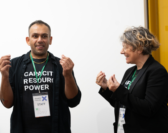 Two people wearing 'Capacity, Resource, Power' t-shirts are presenting work.