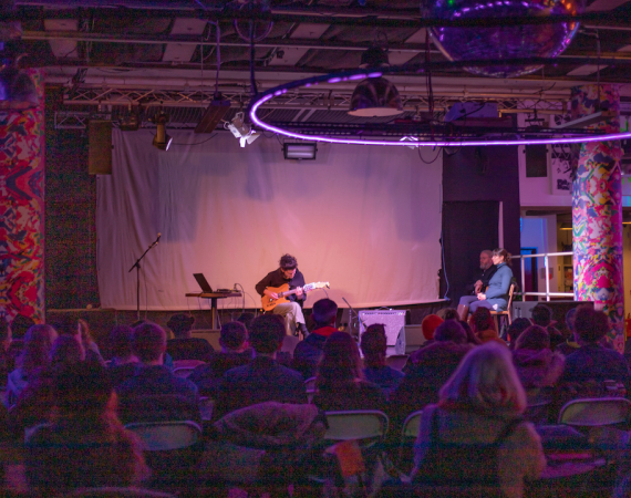 Image of Craig Scott performing on the semi-automated guitar to a small crowd of seated people