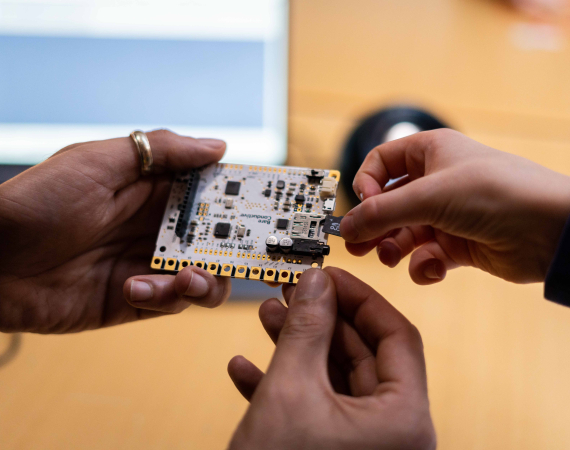 Three hands hold a small circuit board