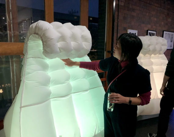 A woman standing in the Pervasive Media Studio, reaching out to touch a large glowing inflatable robot