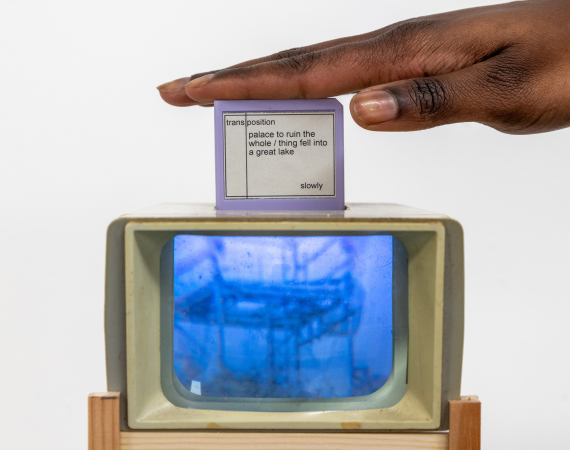 A hand rests on a small screen displaying text. Below, an old TV sits on a wooden stand, showing an abstract blue image. The scene feels nostalgic and artistic.