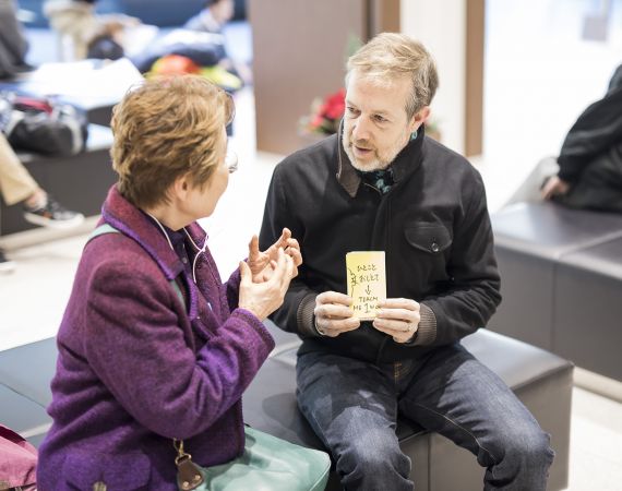 Image of White Man holding text saying "teach me one word" to Japanese Lady