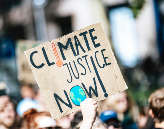Photo of a cardboard placard at a climate rally saying Climate Justice Now