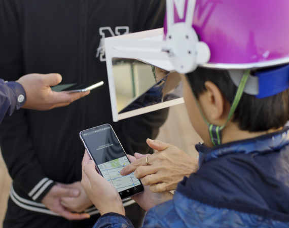Image of person wearing helmet and mirror holding a phone showing a map. Image from Playable City Seoul by Jon Aitken