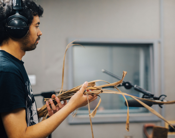 Man with headphones standing in front of microphone with dried reed leaves in his hands