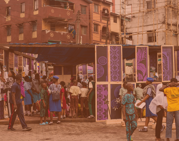 A picture from a project called Meet at the Square. A brightly coloured wooden structure in Lagos. People standing in and around the structure. 