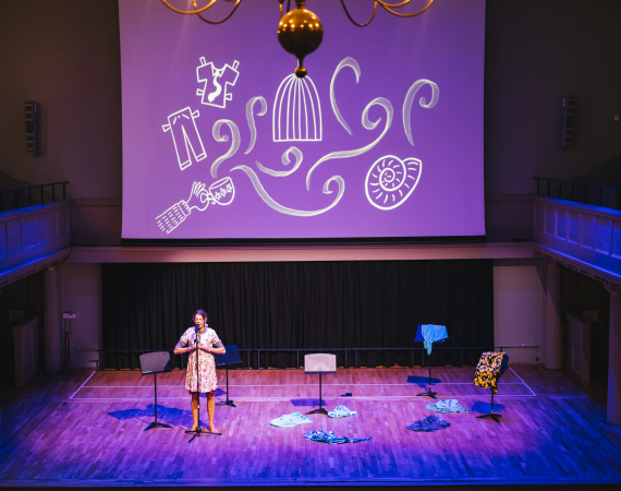Performer on stage with drawings projected on a screen above