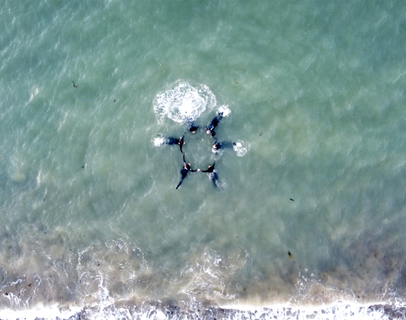 Aerial view of 6 dancers holding a circle shape in the Irish Sea