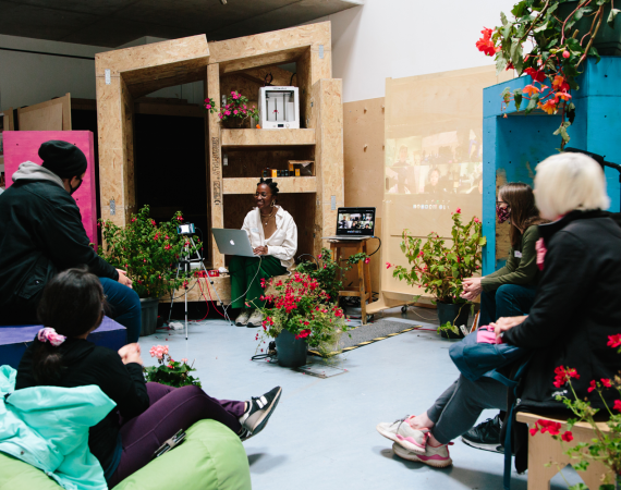 A group of people sitting in a workshop room filled with plants