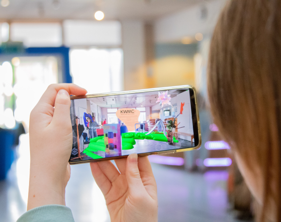 Person photographed from behind holding a phone with an augmented image of the space they are in.