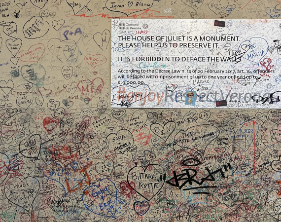 A wall covered in scribbled names and hearts. With a notice asking people not to deface the wall. 