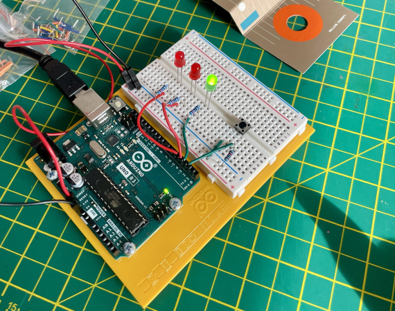 An arduino microcontroller with one green LED lit up and two red LEDs dormant - on a green cutting board background.