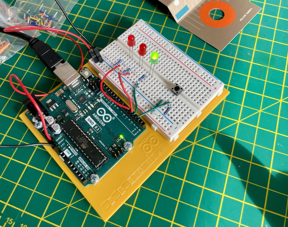 An arduino microcontroller with one green LED lit up and two red LEDs dormant - on a green cutting board background.