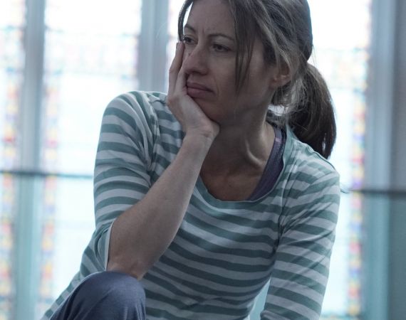 An image of Holly Thomas, a white women, wearing a striped blue and white t-shirt, with shoulder length hair, looking pensive into the distance.