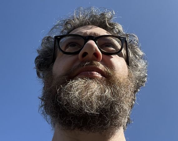 A hairy man's head staring into the distance with blue sky behind