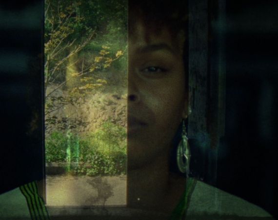 A faded image of a black woman with silver earrings and in traditional Somali dress superimposed onto the entrance of a dark building looking out onto plants and trees.