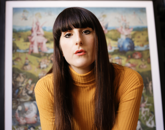 Picture of a woman with brown hair and a fringe, and a yellow jumper. 