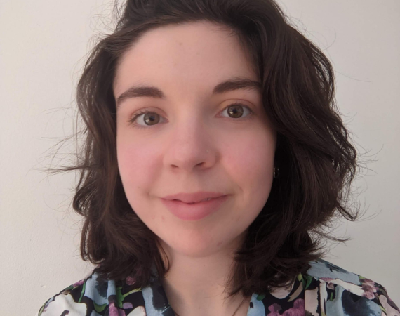 A headshot of a young white woman with shoulder length brown hair in a floral shirt.