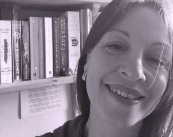 Black and white photo of dark haired white woman smiling with bookshelf behind her