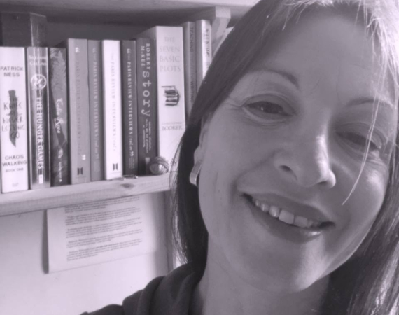 Black and white photo of dark haired white women smiling with book on shelf behind her