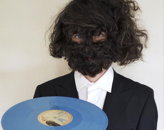 Image of Craig Scott with a hairy face holding a blue record. 