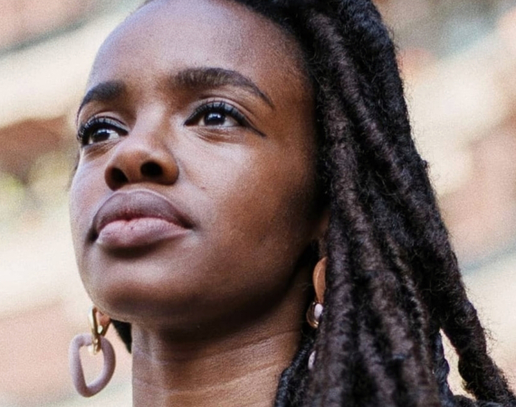 A headshot of Alisha taken from a low angle. They look into the distance beyond the camera.