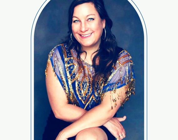 A head and shoulders shot of Caroline who is smiling facing the camera, she has brown hair and a blue and gold sparkly top. 