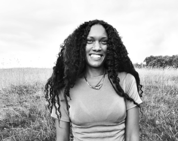 A black and white head and shoulders shot of Natalie who is looking at the camera smiling. 