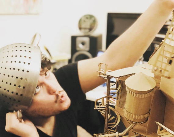 In this picture you can see Leigh Davies sat with a metal collander on his head, handling one of his interactive cardboard sound sculptures from the Playces series.