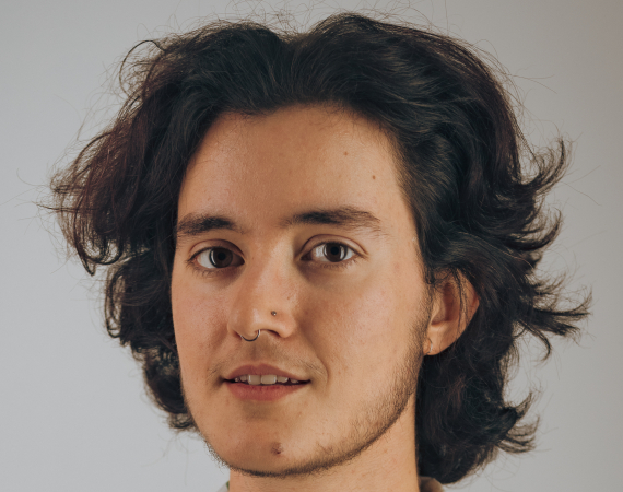 A person in their late 20s with brown hair, short stubble and a shirt with a leaf pattern.