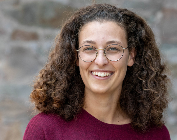 A head-and-shoulders photo of Julia, a white woman with brown curly hair, glasses, laughing, and wearing a red top.