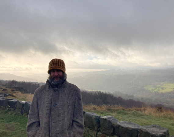 A man with a beard in a wooly hat on a hill in the rain