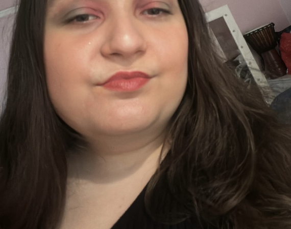An image of a young woman with shoulder length dark brown hair and brown eyes wearing colourful makeup.