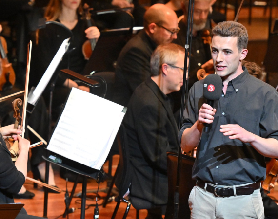 Liam speaking in front of an orchestra
