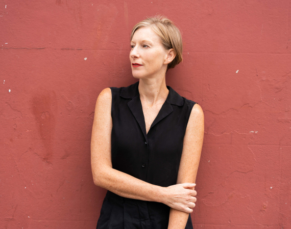 Jo stands in front of a red brown wall.