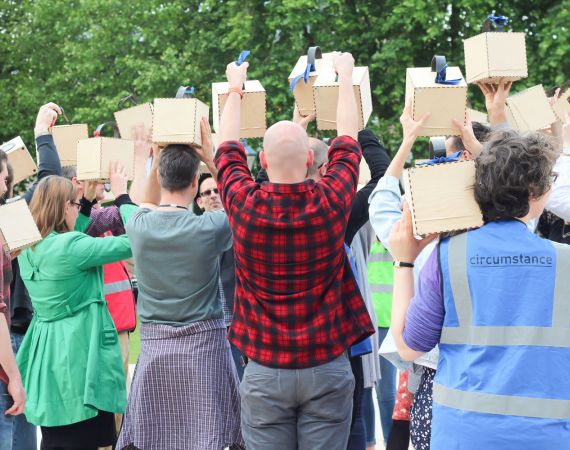 Photo of a group of people with their backs to the camera holding audio speakers in the air