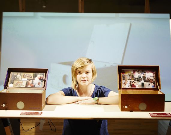 Chloe a white queer woman in her 30s is next to two music memory boxes, her project for people living with dementia. 